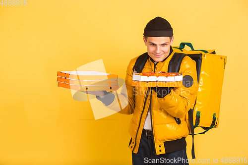 Image of Contacless delivery service during quarantine. Man delivers food and shopping bags during insulation. Emotions of deliveryman isolated on yellow background.