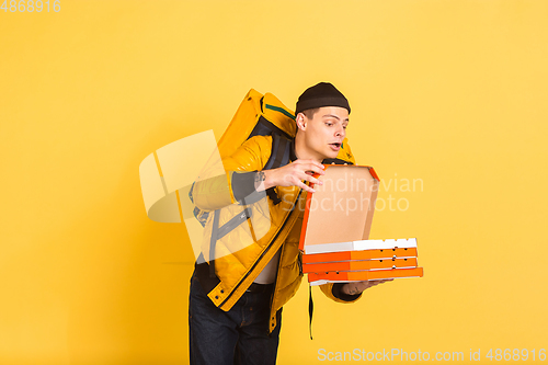 Image of Contacless delivery service during quarantine. Man delivers food and shopping bags during insulation. Emotions of deliveryman isolated on yellow background.