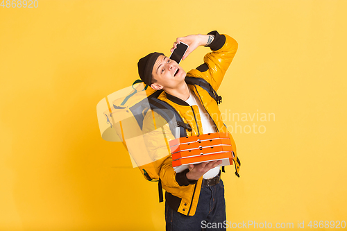 Image of Contacless delivery service during quarantine. Man delivers food and shopping bags during insulation. Emotions of deliveryman isolated on yellow background.