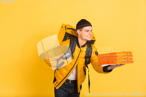 Image of Contacless delivery service during quarantine. Man delivers food and shopping bags during insulation. Emotions of deliveryman isolated on yellow background.