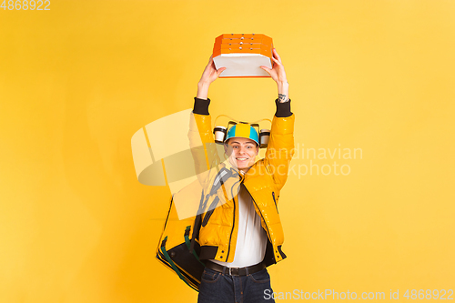 Image of Contacless delivery service during quarantine. Man delivers food and shopping bags during insulation. Emotions of deliveryman isolated on yellow background.