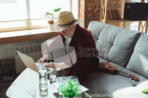 Image of Mature senior older man during quarantine, realizing how important stay at home during virus outbreak, giving concert of taking online lessons of guitar playing