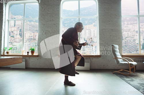 Image of Mature senior older man during quarantine, realizing how important stay at home during virus outbreak, giving concert of taking online lessons of guitar playing in Monte Carlo