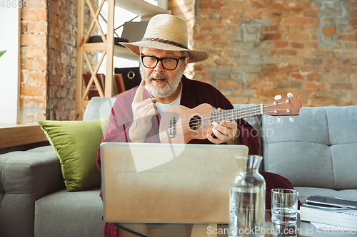 Image of Mature senior older man during quarantine, realizing how important stay at home during virus outbreak, giving concert of taking online lessons of guitar playing