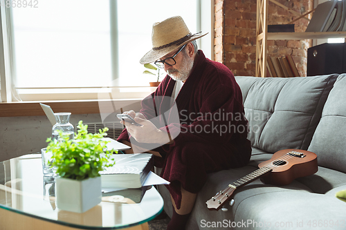 Image of Mature senior older man during quarantine, realizing how important stay at home during virus outbreak, giving concert of taking online lessons of guitar playing