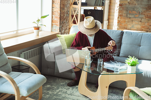 Image of Mature senior older man during quarantine, realizing how important stay at home during virus outbreak, giving concert of taking online lessons of guitar playing