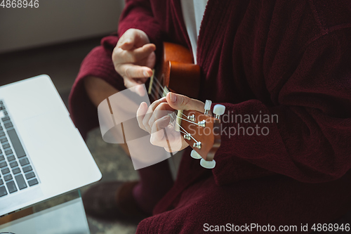 Image of Mature senior older man during quarantine, virus outbreak, giving concert of taking online lessons of guitar playing, close up of hands