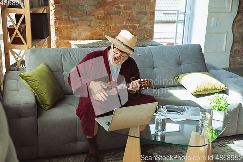 Image of Mature senior older man during quarantine, realizing how important stay at home during virus outbreak, giving concert of taking online lessons of guitar playing