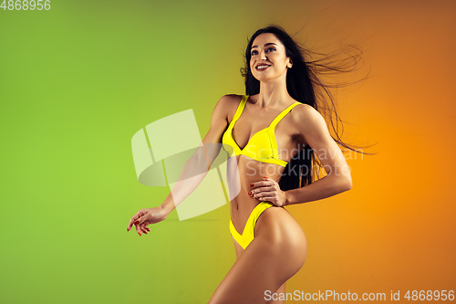 Image of Fashion portrait of young fit and sportive woman in stylish yellow luxury swimwear on gradient background. Perfect body ready for summertime.