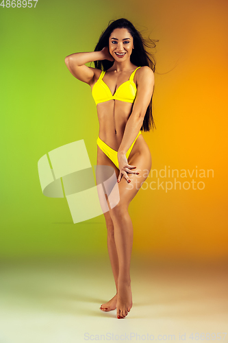 Image of Fashion portrait of young fit and sportive woman in stylish yellow luxury swimwear on gradient background. Perfect body ready for summertime.