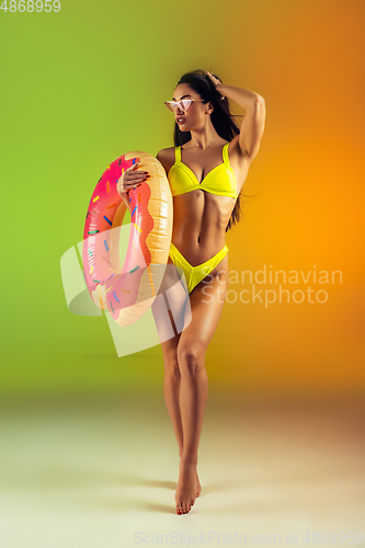 Image of Fashion portrait of young fit and sportive woman with rubber donut in stylish yellow swimwear on gradient background. Perfect body ready for summertime.