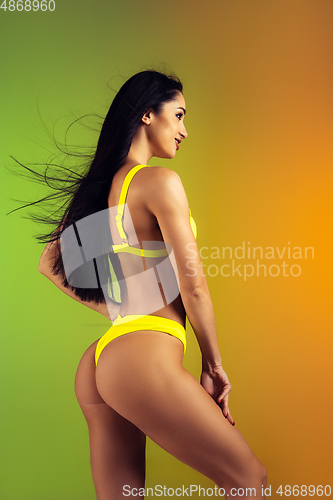 Image of Fashion portrait of young fit and sportive woman in stylish yellow luxury swimwear on gradient background. Perfect body ready for summertime.