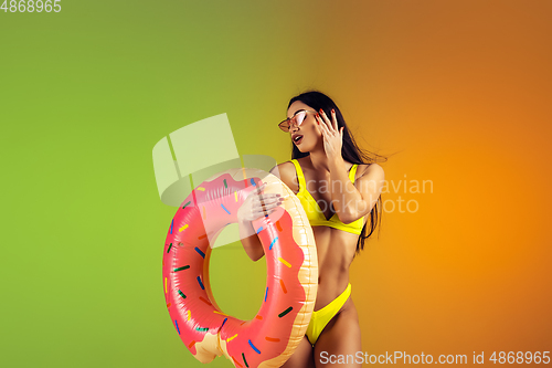 Image of Fashion portrait of young fit and sportive woman with rubber donut in stylish yellow swimwear on gradient background. Perfect body ready for summertime.