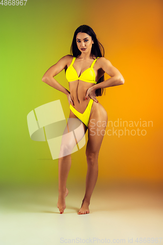 Image of Fashion portrait of young fit and sportive woman in stylish yellow luxury swimwear on gradient background. Perfect body ready for summertime.