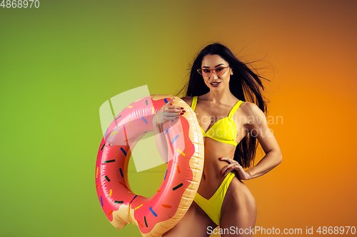 Image of Fashion portrait of young fit and sportive woman with rubber donut in stylish yellow swimwear on gradient background. Perfect body ready for summertime.