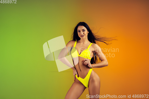 Image of Fashion portrait of young fit and sportive woman in stylish yellow luxury swimwear on gradient background. Perfect body ready for summertime.