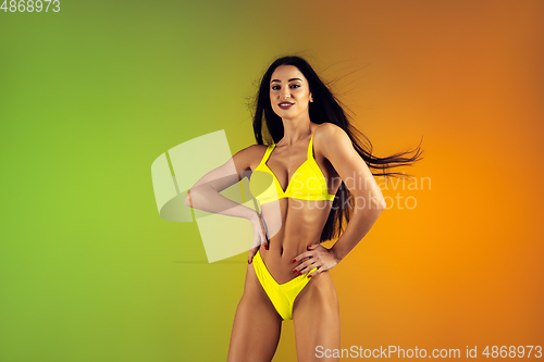 Image of Fashion portrait of young fit and sportive woman in stylish yellow luxury swimwear on gradient background. Perfect body ready for summertime.