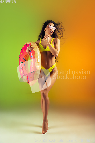 Image of Fashion portrait of young fit and sportive woman with rubber donut in stylish yellow swimwear on gradient background. Perfect body ready for summertime.