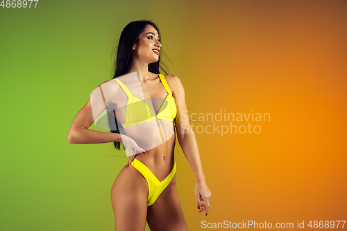 Image of Fashion portrait of young fit and sportive woman in stylish yellow luxury swimwear on gradient background. Perfect body ready for summertime.