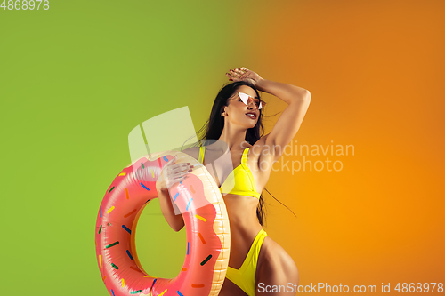 Image of Fashion portrait of young fit and sportive woman with rubber donut in stylish yellow swimwear on gradient background. Perfect body ready for summertime.