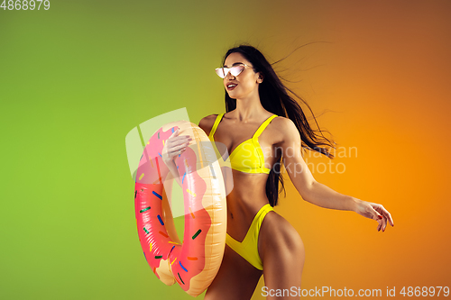 Image of Fashion portrait of young fit and sportive woman with rubber donut in stylish yellow swimwear on gradient background. Perfect body ready for summertime.