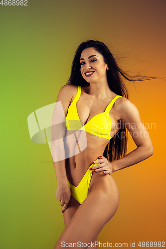 Image of Fashion portrait of young fit and sportive woman in stylish yellow luxury swimwear on gradient background. Perfect body ready for summertime.