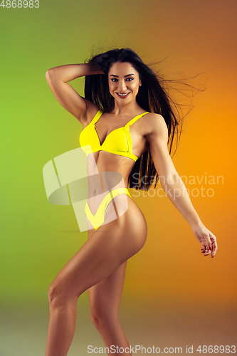 Image of Fashion portrait of young fit and sportive woman in stylish yellow luxury swimwear on gradient background. Perfect body ready for summertime.