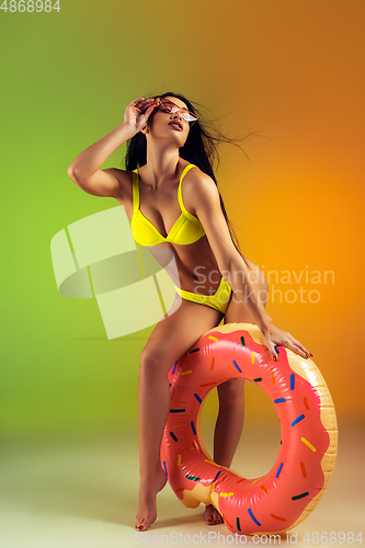 Image of Fashion portrait of young fit and sportive woman with rubber donut in stylish yellow swimwear on gradient background. Perfect body ready for summertime.