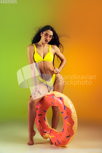 Image of Fashion portrait of young fit and sportive woman with rubber donut in stylish yellow swimwear on gradient background. Perfect body ready for summertime.