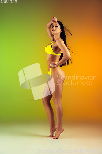 Image of Fashion portrait of young fit and sportive woman in stylish yellow luxury swimwear on gradient background. Perfect body ready for summertime.