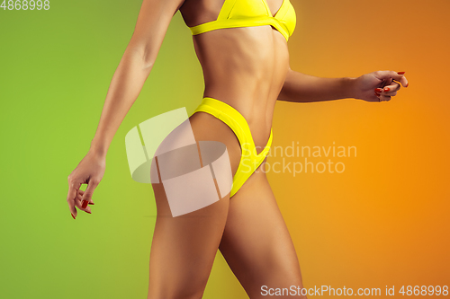 Image of Close up of young fit and sportive woman in stylish yellow swimwear on gradient background. Perfect body ready for summertime.