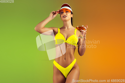 Image of Fashion portrait of young fit and sportive woman with cocktail in stylish yellow luxury swimwear on gradient background. Perfect body ready for summertime.