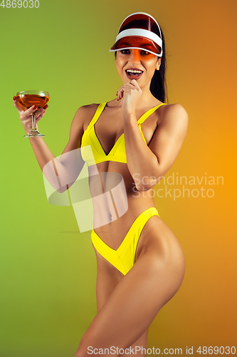 Image of Fashion portrait of young fit and sportive woman with cocktail in stylish yellow luxury swimwear on gradient background. Perfect body ready for summertime.