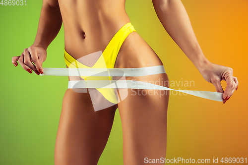 Image of Close up of young fit and sportive woman with measurer in stylish yellow swimwear on gradient background. Perfect body ready for summertime.