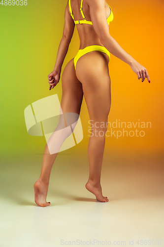 Image of Close up of young fit and sportive woman in stylish yellow swimwear on gradient background. Perfect body ready for summertime.