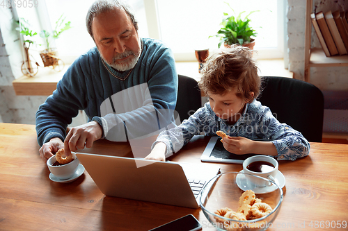 Image of Grandfather and his grandson spending time insulated at home, stadying, watching cinema, shopping together