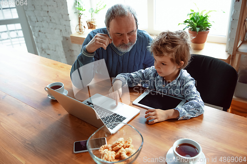 Image of Grandfather and his grandson spending time insulated at home, stadying, watching cinema, shopping together