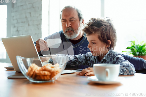 Image of Grandfather and his grandson spending time insulated at home, stadying, watching cinema, shopping together