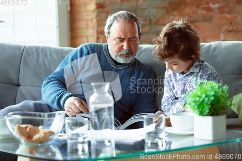 Image of Grandfather and his grandson spending time insulated at home, having fun, reading magazine together, happy