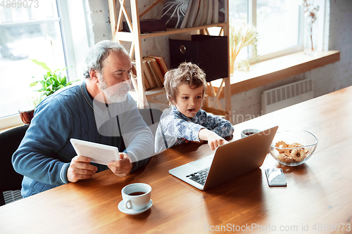 Image of Grandfather and his grandson spending time insulated at home, stadying, watching cinema, shopping together