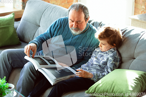 Image of Grandfather and his grandson spending time insulated at home, having fun, reading magazine together, happy