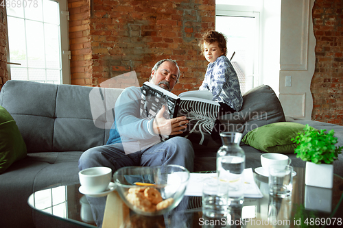 Image of Grandfather and his grandson spending time insulated at home, having fun, reading magazine together, happy