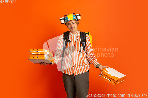 Image of Contacless delivery service during quarantine. Man delivers food and shopping bags during insulation. Emotions of deliveryman isolated on orange background.