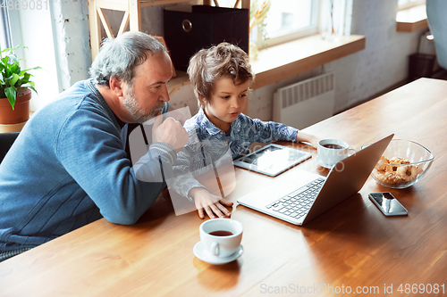 Image of Grandfather and his grandson spending time insulated at home, stadying, watching cinema, shopping together