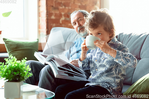 Image of Grandfather and his grandson spending time insulated at home, having fun, reading magazine together, happy