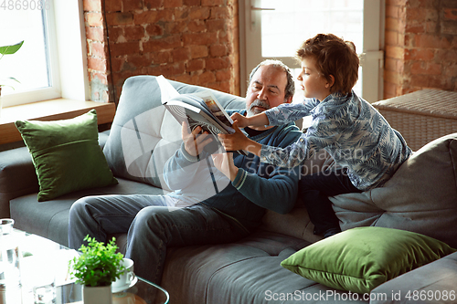 Image of Grandfather and his grandson spending time insulated at home, having fun, reading magazine together, happy