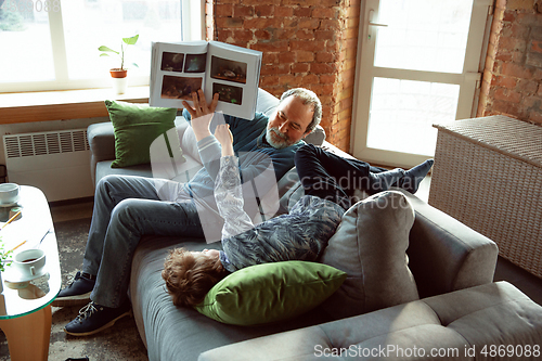 Image of Grandfather and his grandson spending time insulated at home, having fun, reading magazine together, happy