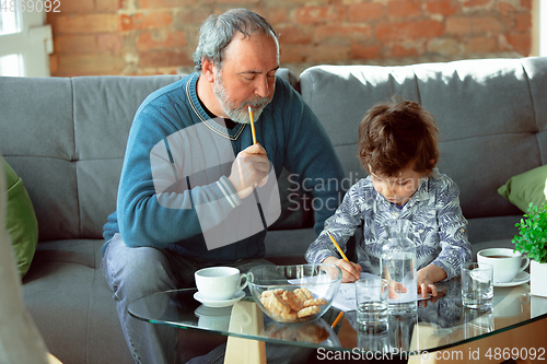 Image of Grandfather and his grandson spending time insulated at home, stadying, writing, drawing or playing together