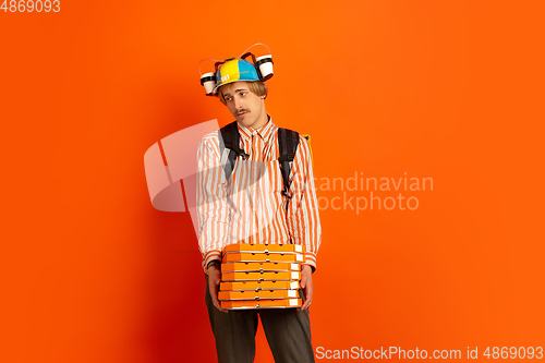 Image of Contacless delivery service during quarantine. Man delivers food and shopping bags during insulation. Emotions of deliveryman isolated on orange background.