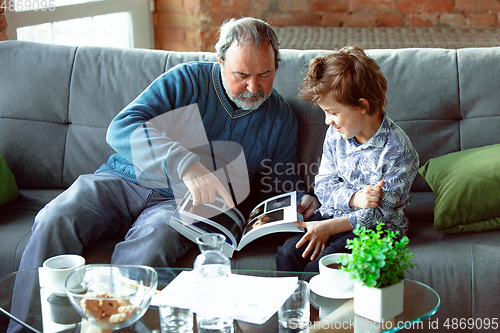 Image of Grandfather and his grandson spending time insulated at home, having fun, reading magazine together, happy